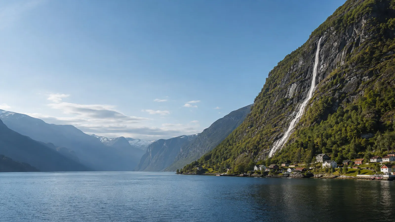 Fjord norvégien profond entre montagnes, cascade et petit village au bord de l'eau