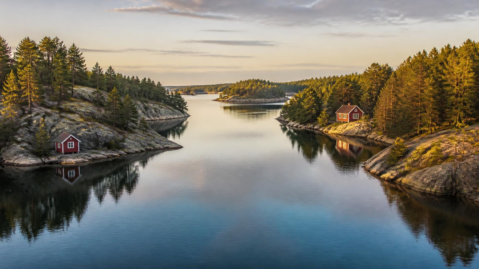 Chenal étroit de l'archipel de Stockholm bordé de rochers de granite, de pins et d'une maison rouge, sous une lumière nordique dorée